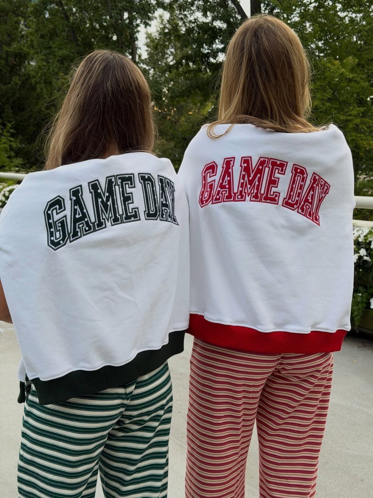 Two women wearing matching Game Day sweatshirts and striped pants from behind.