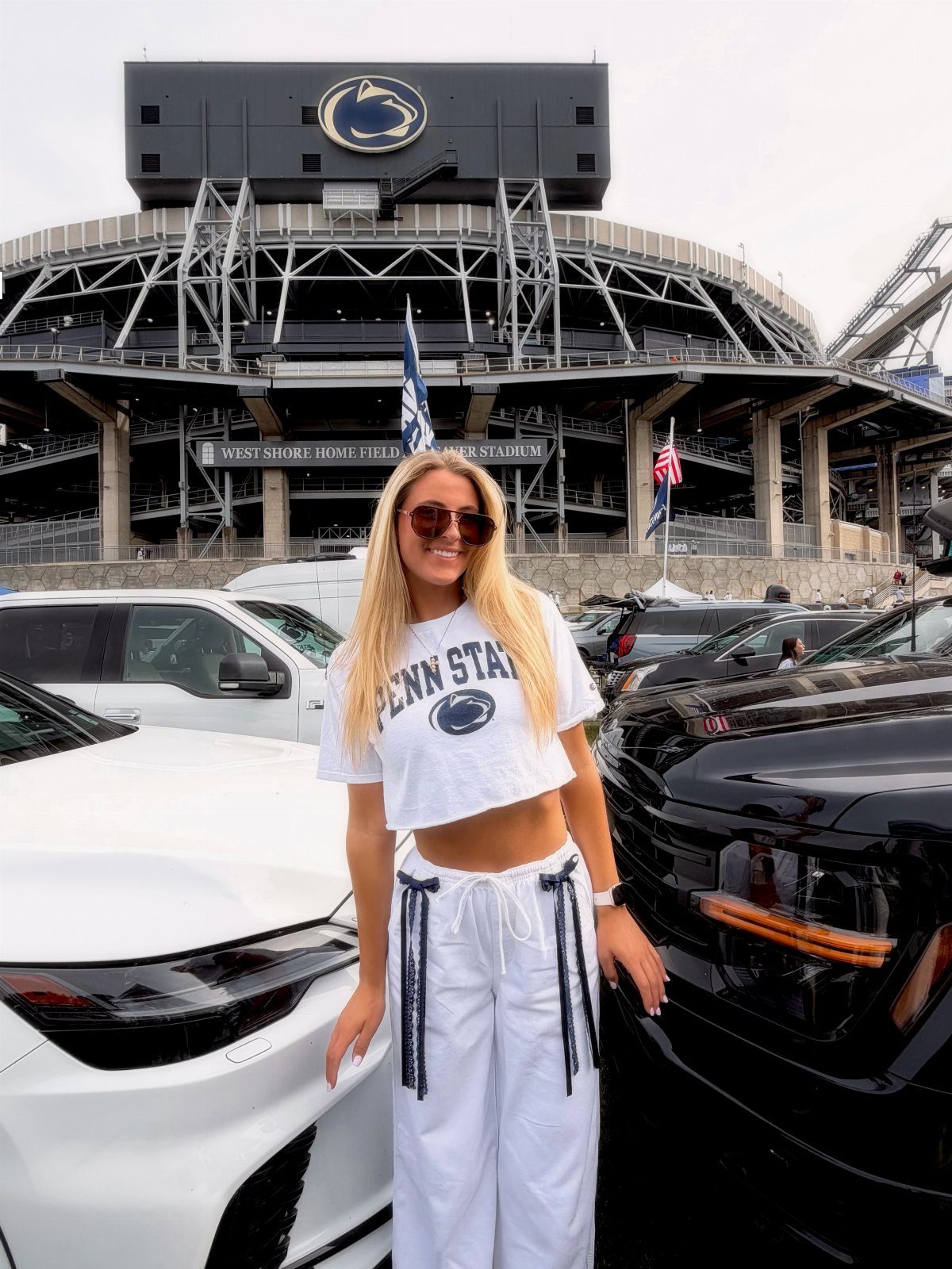 Woman in white cropped Penn State shirt and white pants before a stadium
