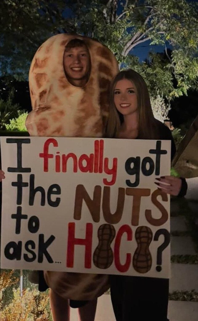 Teenager in peanut costume and girl holding a funny homecoming proposal poster.