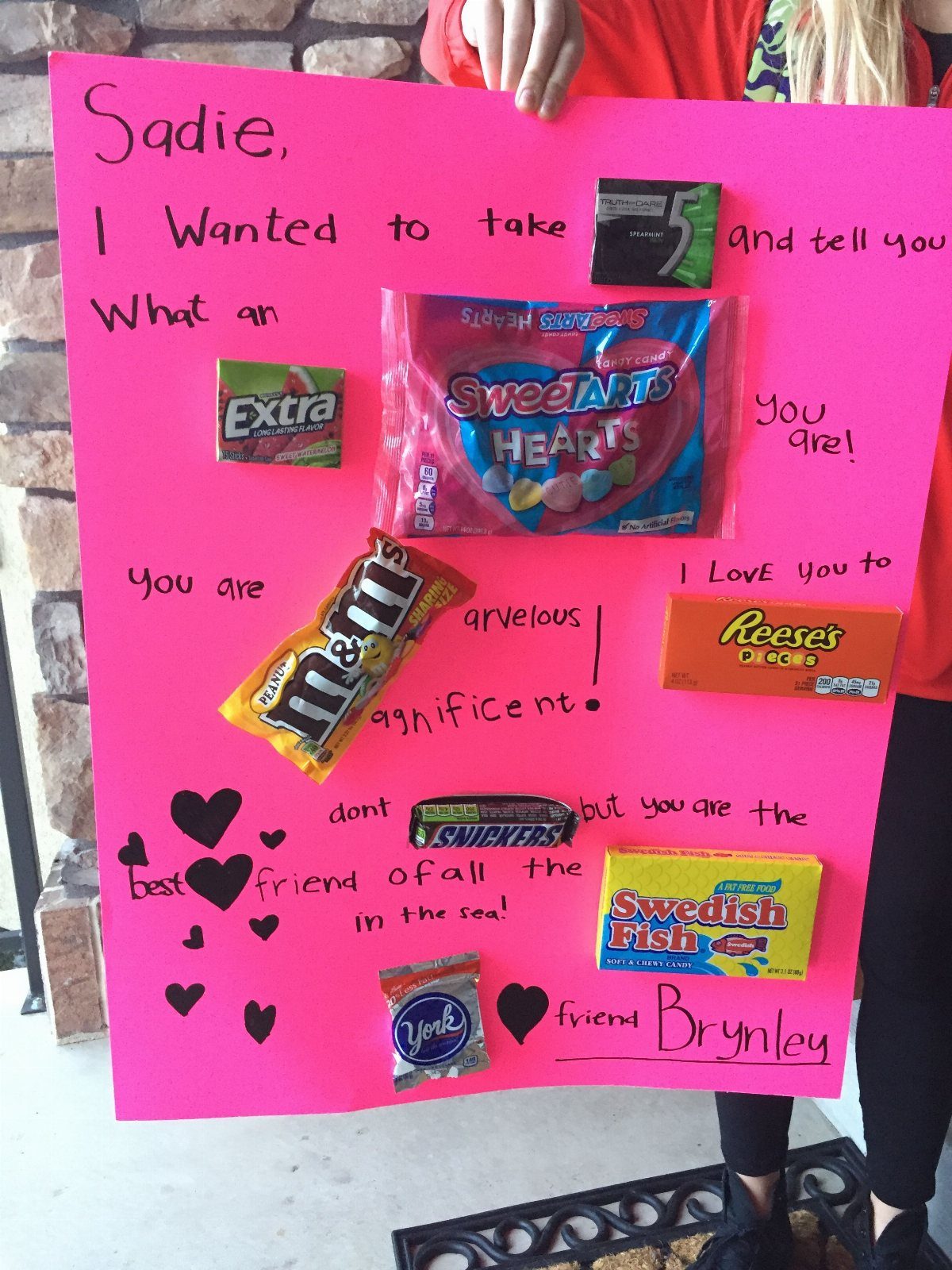 Pink poster with candy bars and handwritten message held by a person.