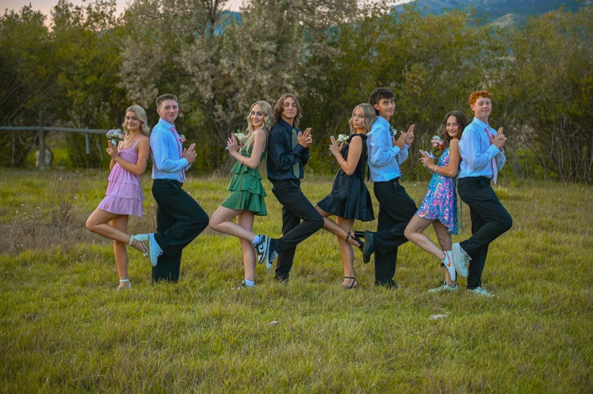 Group of teenagers in prom dresses and suits striking comedic mirrored poses outdoors.