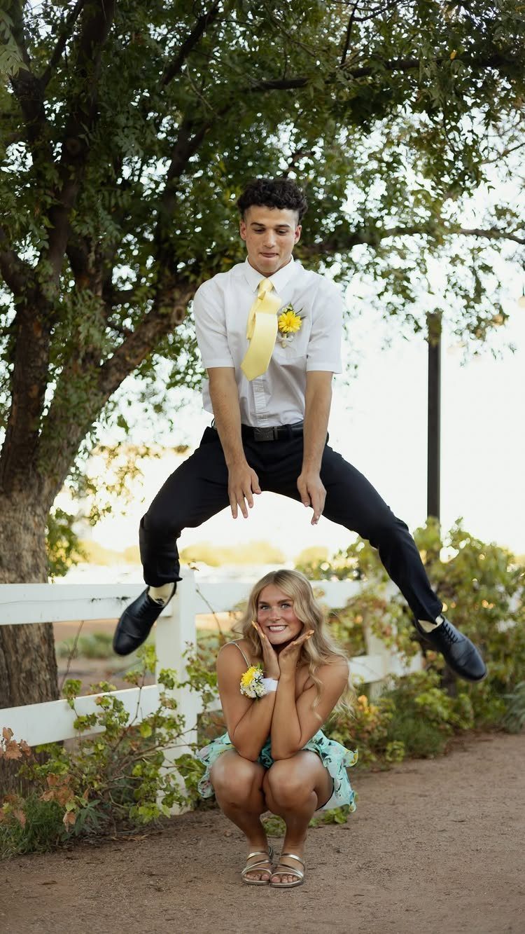 Young man jumping over a crouching young woman in formal prom attire outdoors.