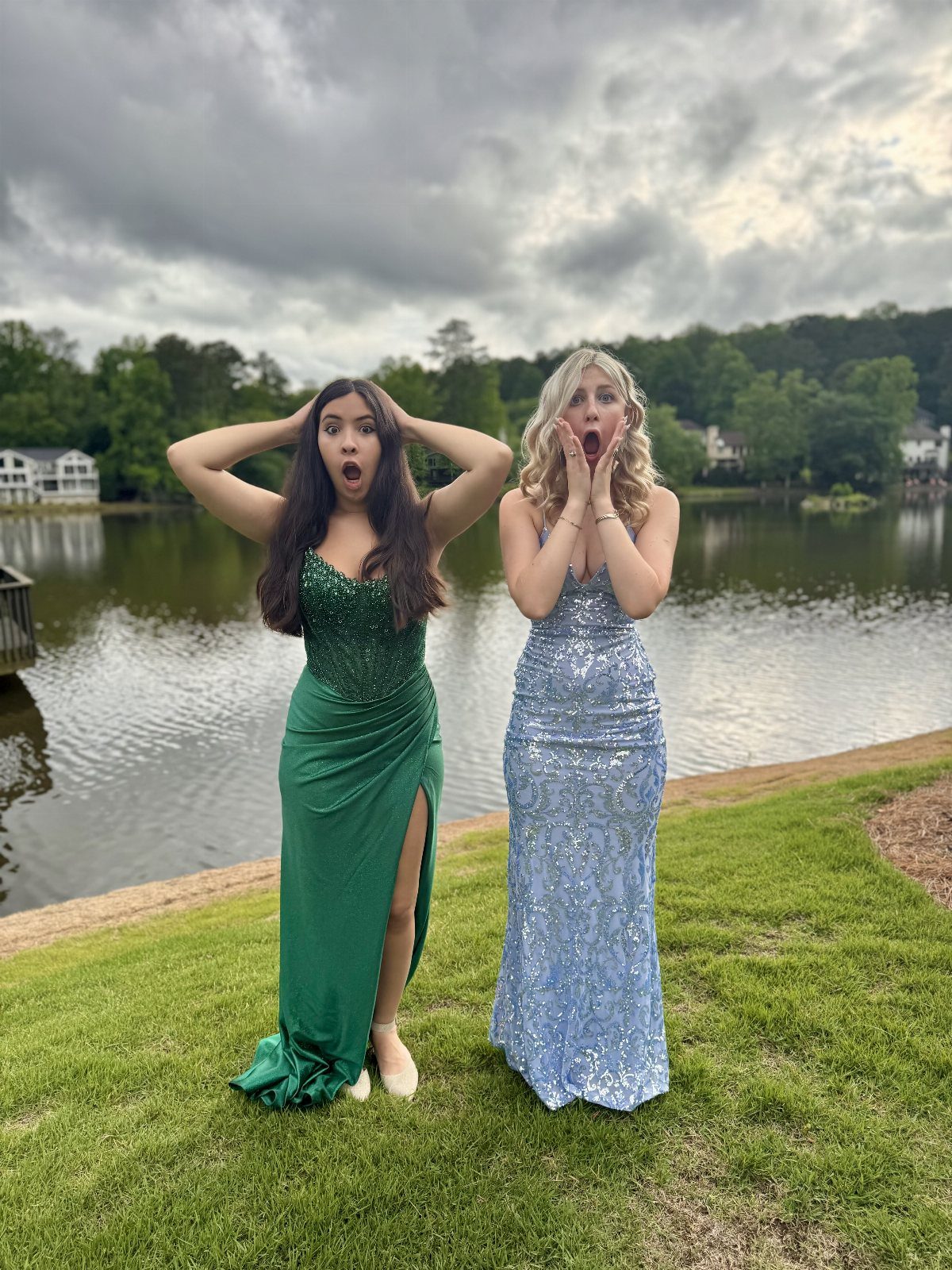 Two women in formal gowns making surprised faces by a lake.