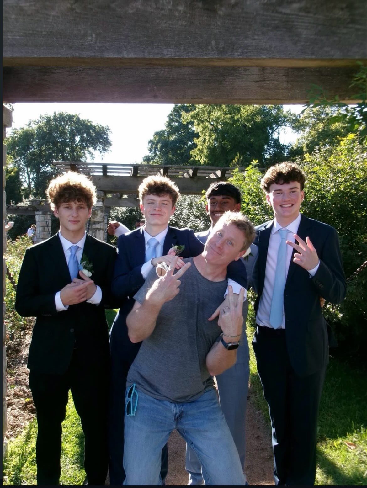 Five young men in suits and casual wear posing together outdoors under wood beams.