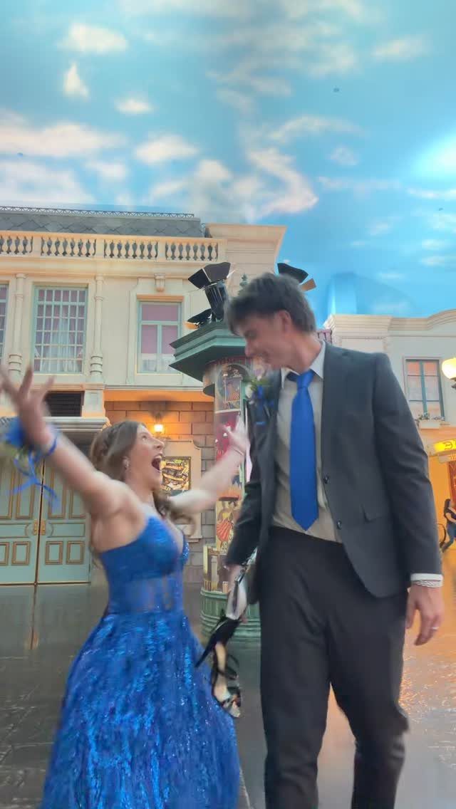 Young couple in formal prom attire posing excitedly in a town setting.