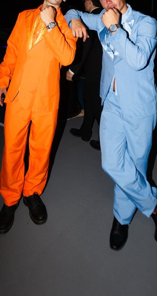 Two men in bright orange and blue suits posing with hands on lapels.