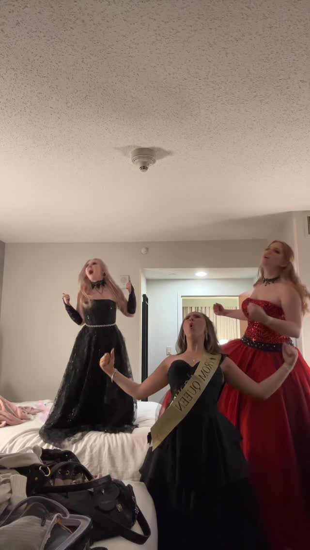 Three young women in formal prom dresses posing and singing in a bedroom