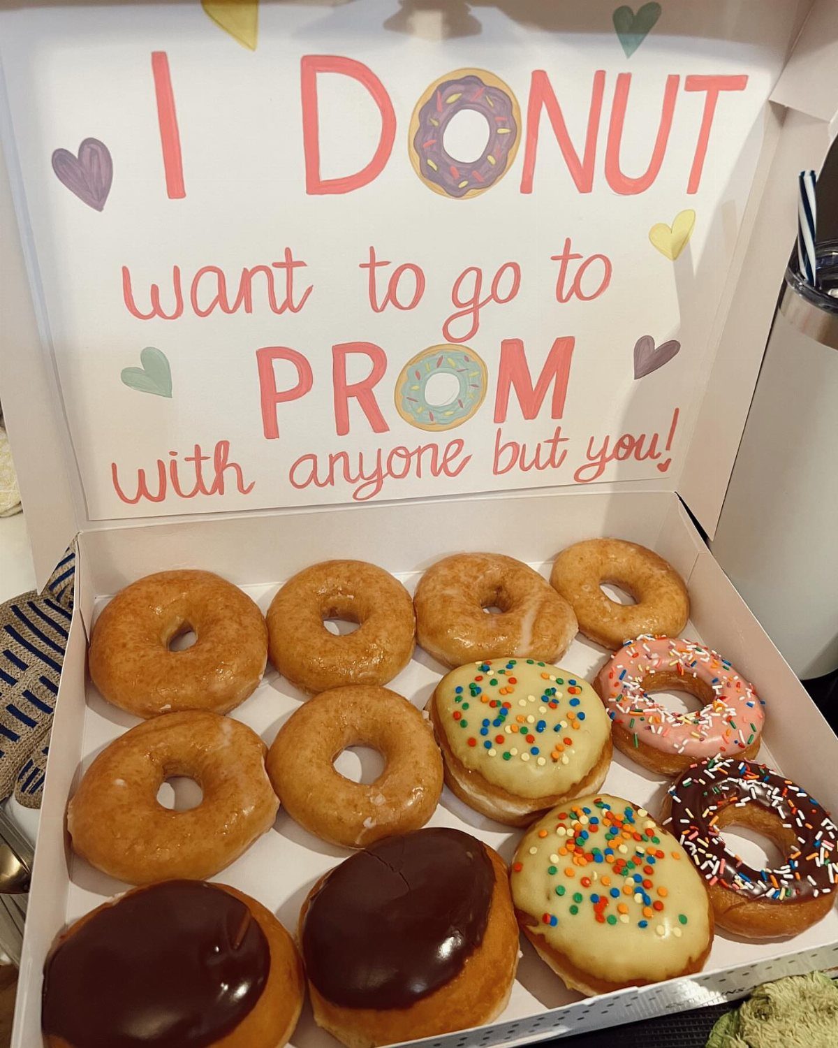 Box of assorted donuts with a handwritten prom proposal sign on the lid