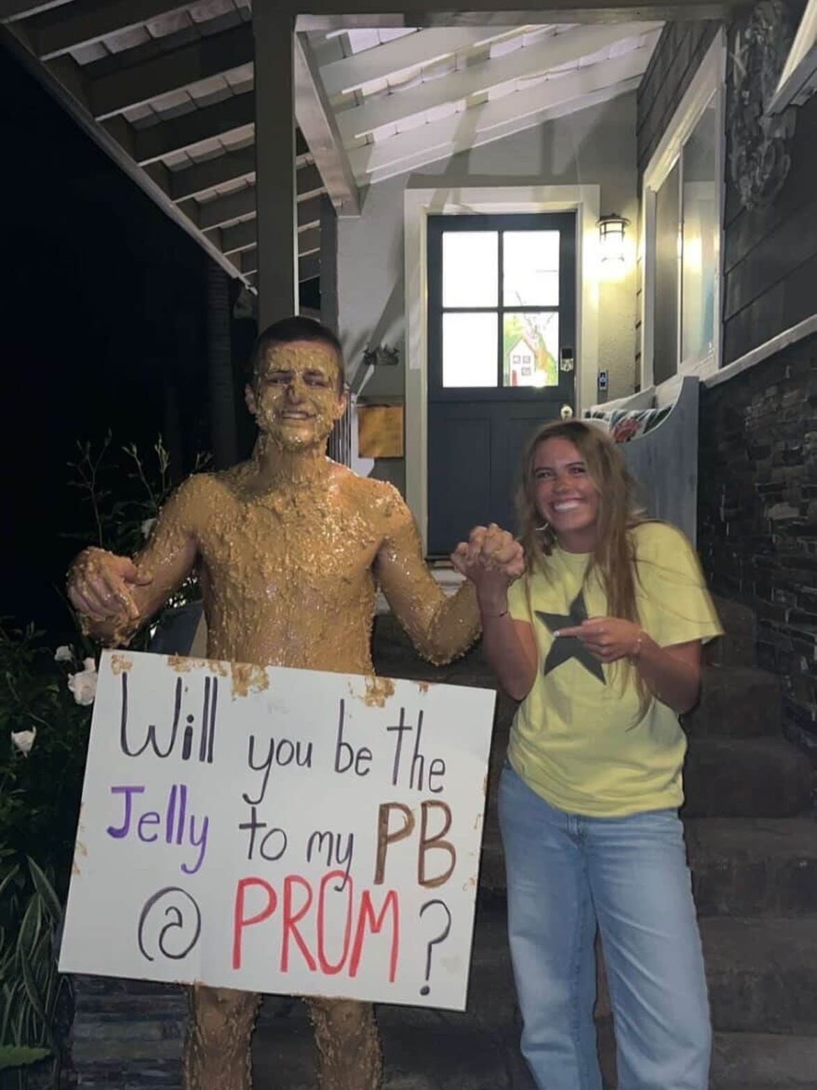 Peanut butter covered boy holding a prom proposal sign next to a smiling girl.