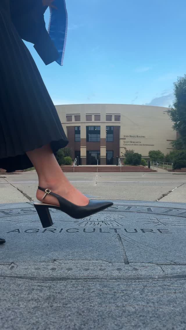 Black pointed-toe slingback heel on a stone pavement with a graduation building background