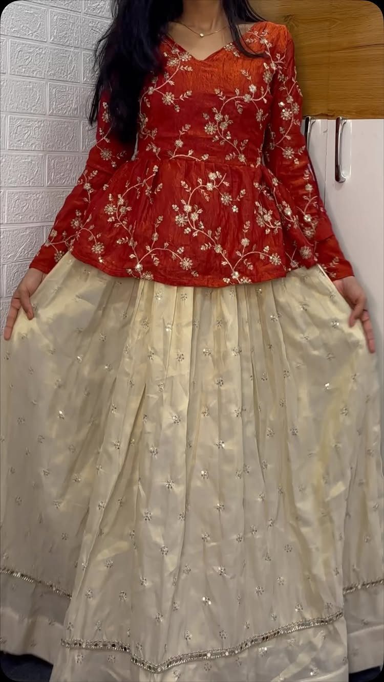 Person wearing a red embroidered top and a voluminous cream-colored floor-length skirt.
