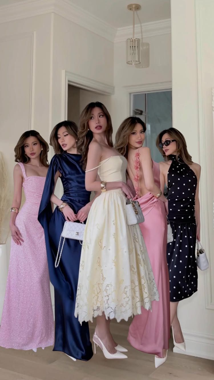 Five women posing in elegant cocktail and formal dresses in a white room.