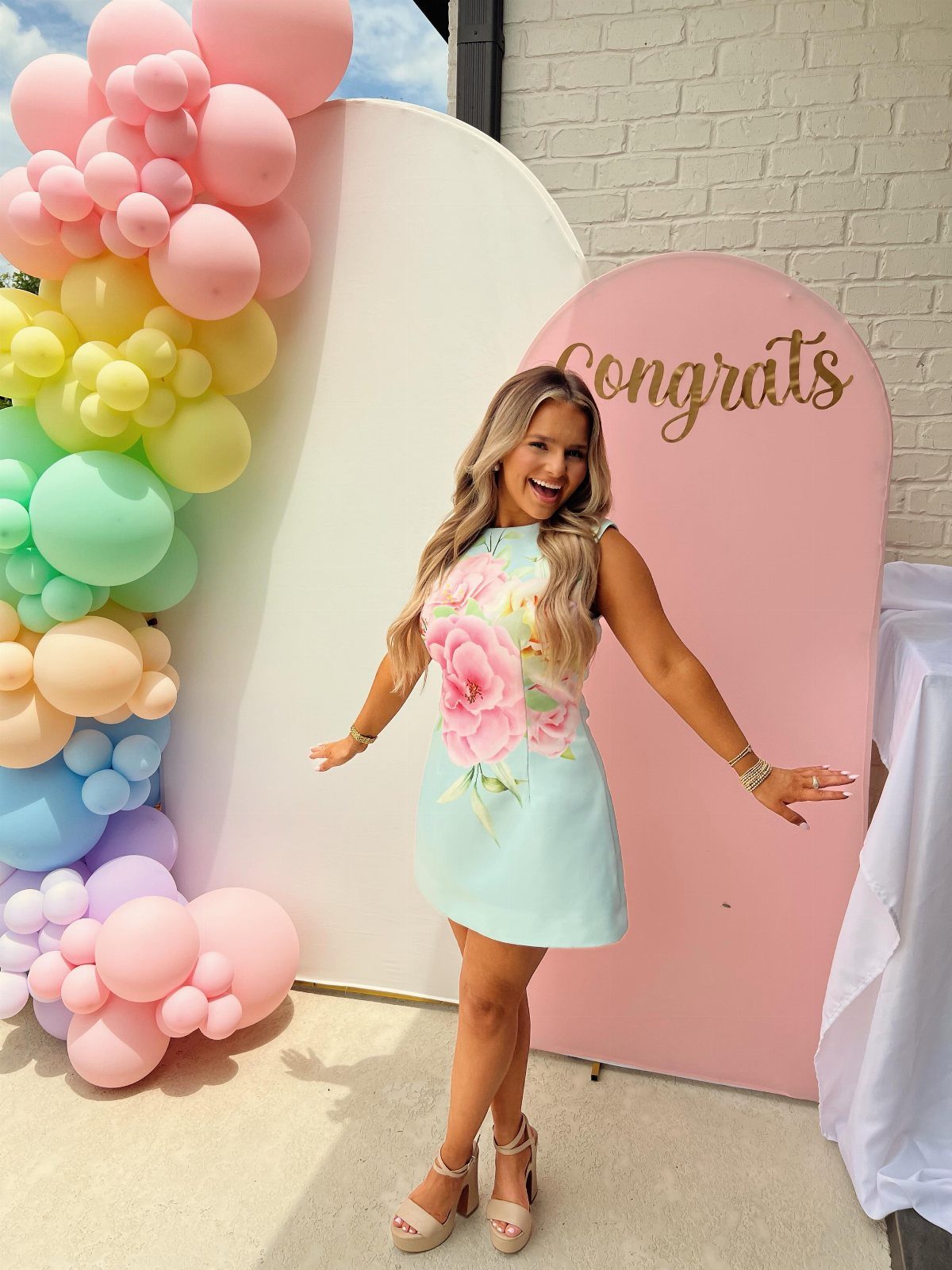 Woman in floral blue dress posing by pastel balloons and Congrats sign