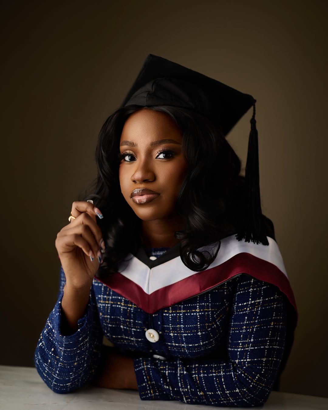Young woman in graduation cap and blue plaid blazer posing in a studio