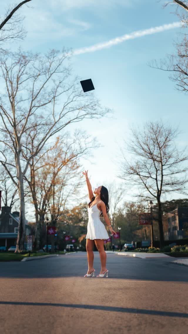 Woman in white dress tossing a black graduation cap into the air on a road