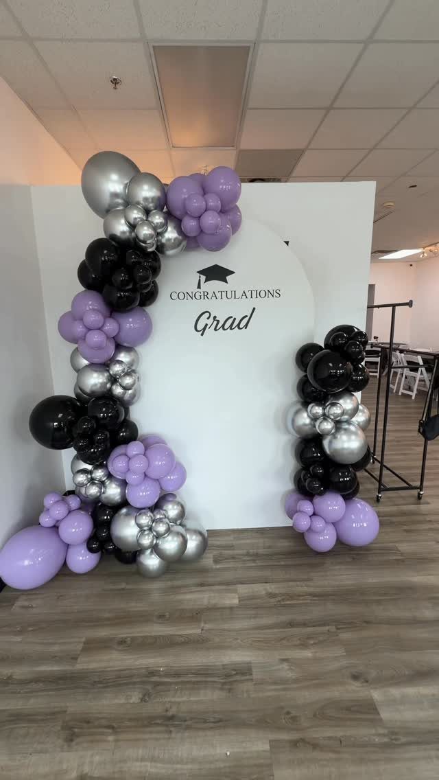 Graduation backdrop with purple, silver, and black balloons and a Congratulations Grad sign.