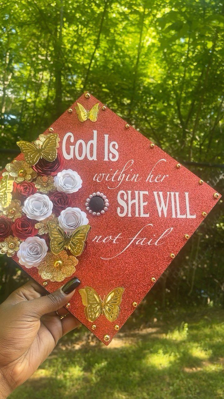 Red glittery graduation cap decorated with paper roses, gold butterflies, and religious text.