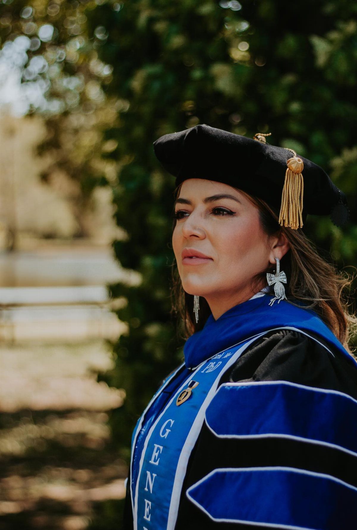 Woman in a black and blue graduation gown and tam posing outdoors.