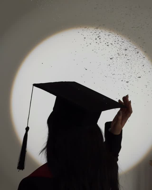 Silhouette of a graduate in cap and gown against a circular light background