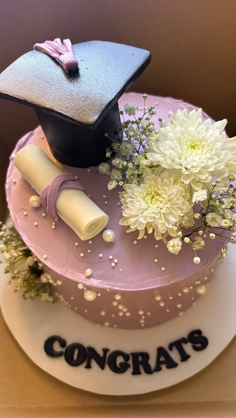 Purple graduation cake topped with a black cap, diploma, and white flowers.