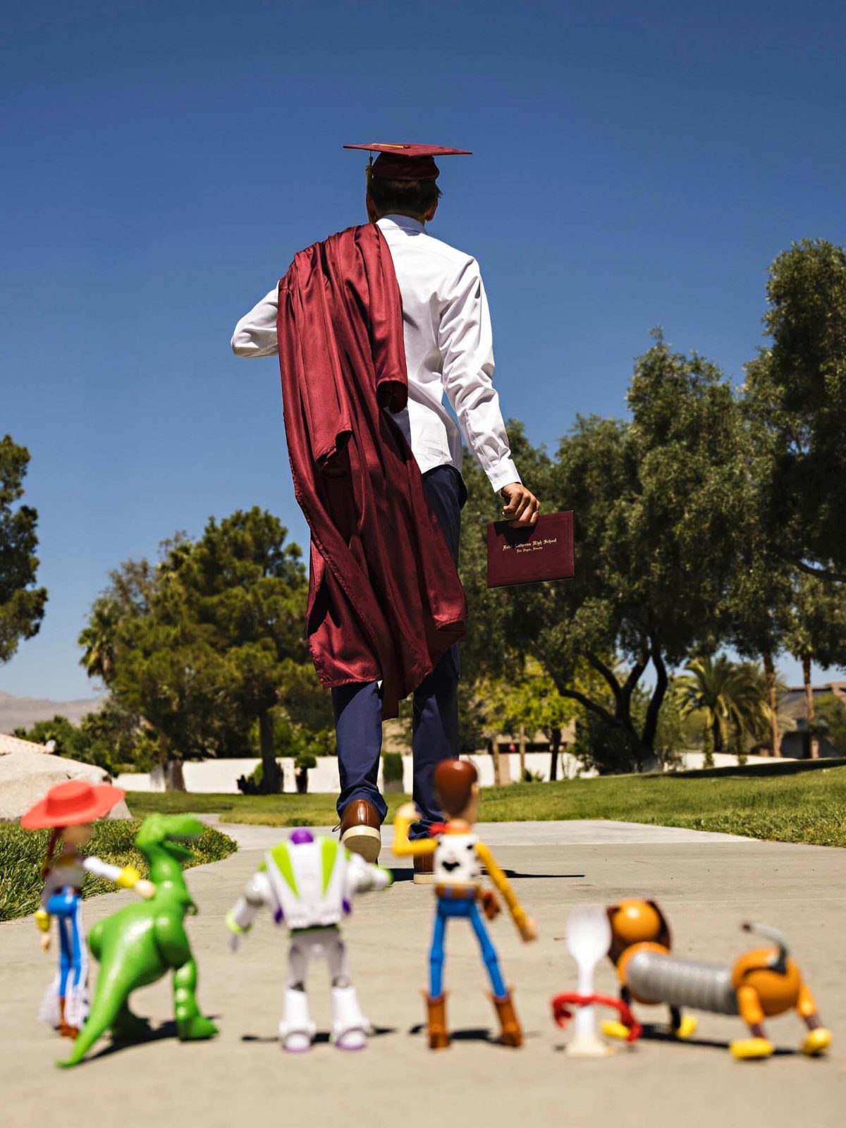 Graduate walking away from Toy Story figures on a sunny paved path