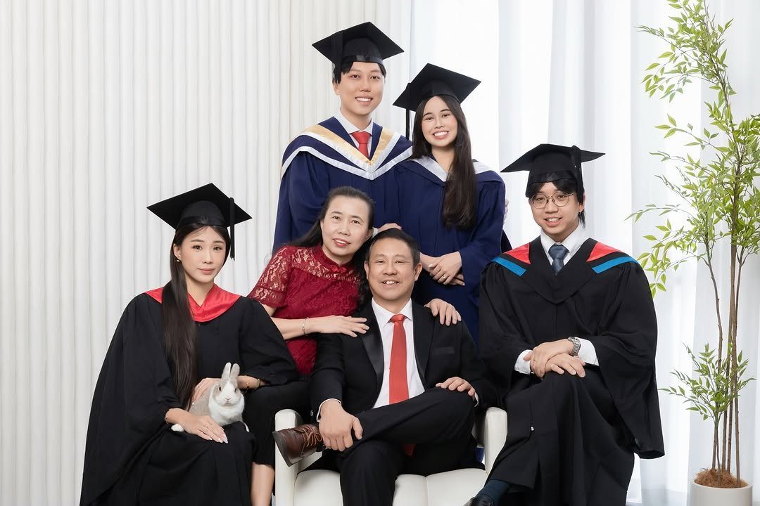 Graduates in caps and gowns posing with their parents in a bright room.