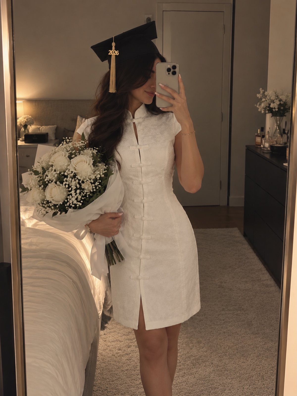 Woman in a short white graduation dress and cap holding white flowers.