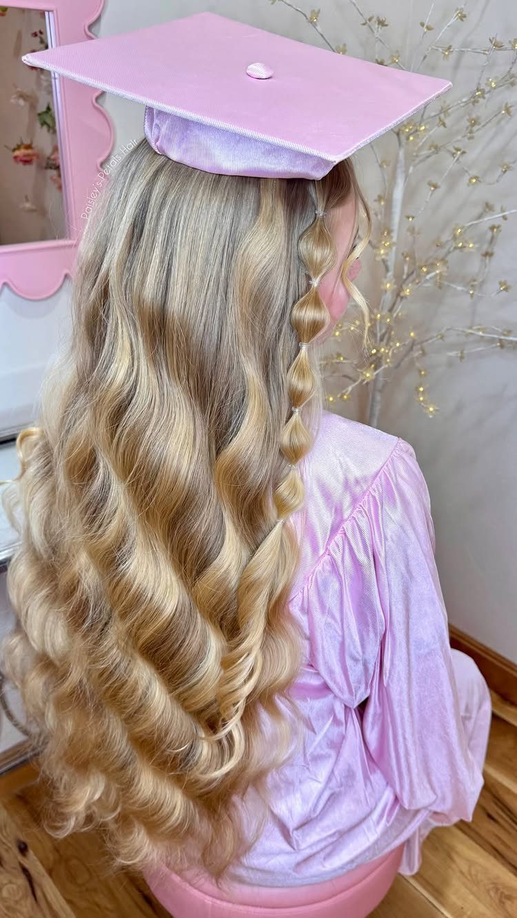 Long blonde curly hair with a small braid under a pink graduation cap.
