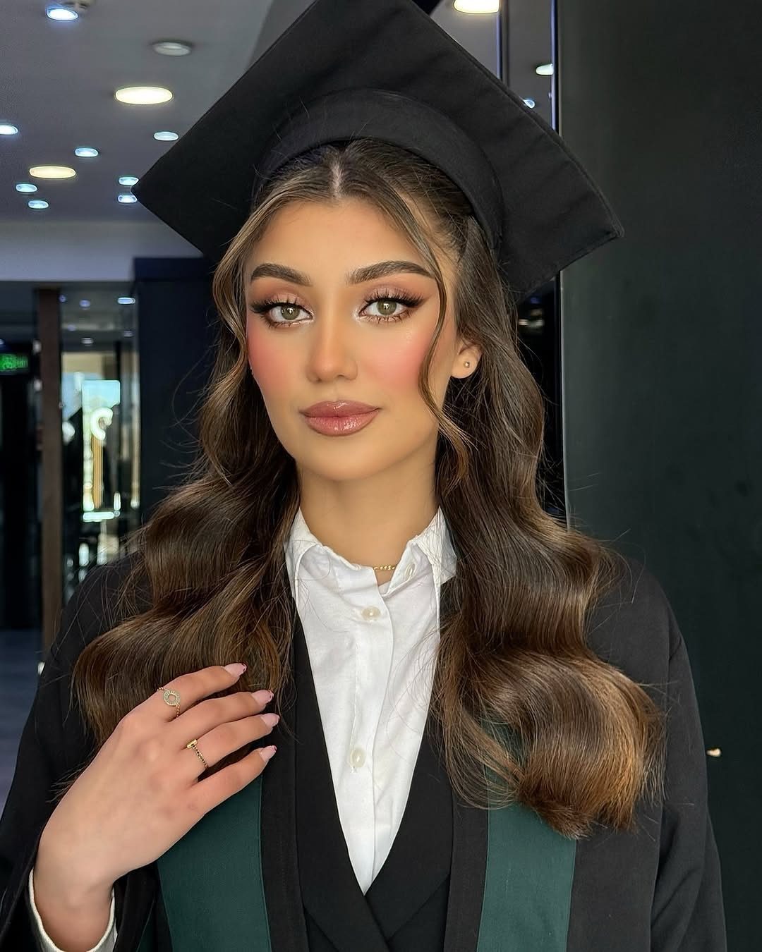 Woman in graduation cap and gown with long brown center-parted loose curls.