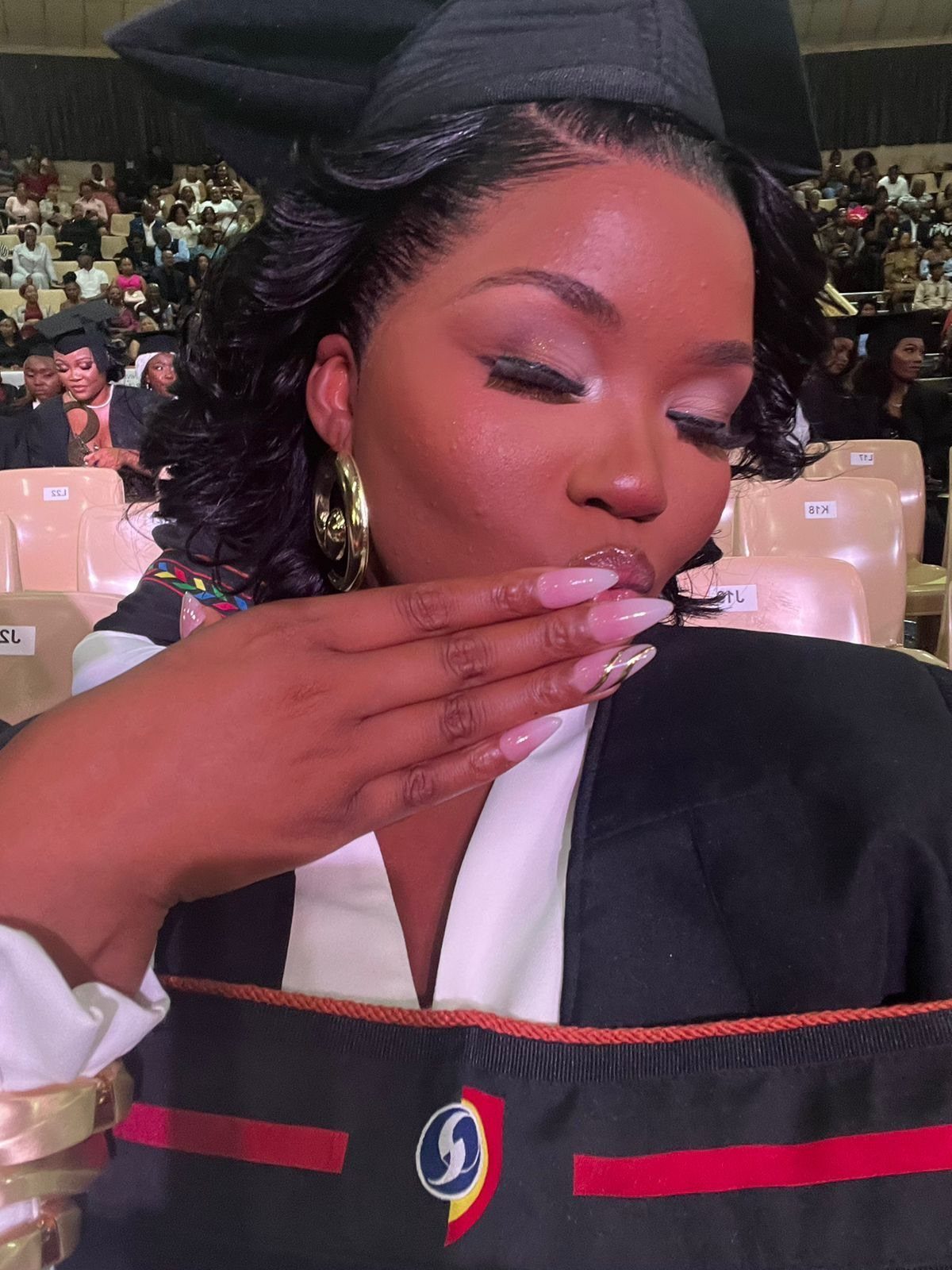 Woman in graduation cap and gown with sleek, polished wavy hair and face-framing edges.