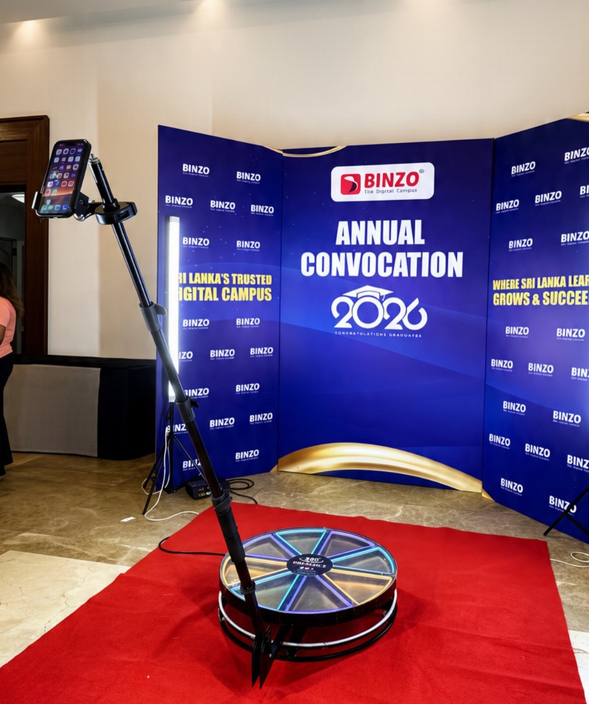 360 photo booth platform with rotating camera arm in front of convocation backdrop