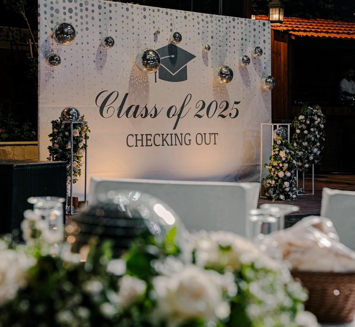 Graduation backdrop with Class of 2025 text, silver balloons, and white floral arrangements.