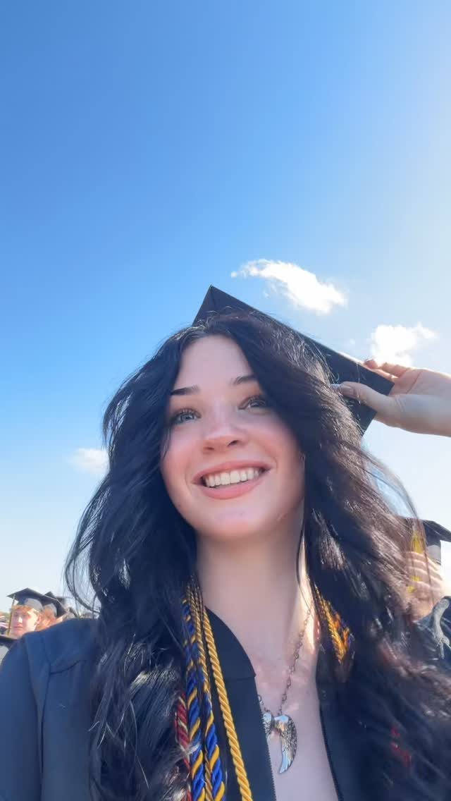 Smiling graduate woman in black gown and cap under a bright blue sky
