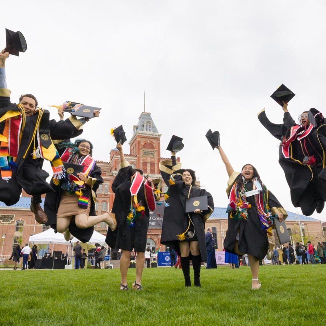 Graduates in gowns jumping and tossing their caps in the air on campus.