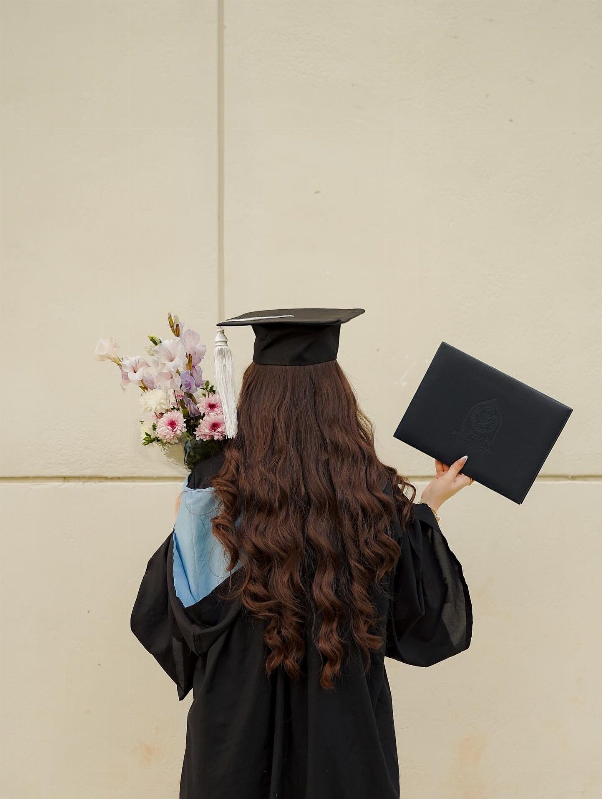 Graduate from behind holding a flower bouquet and a black diploma cover.