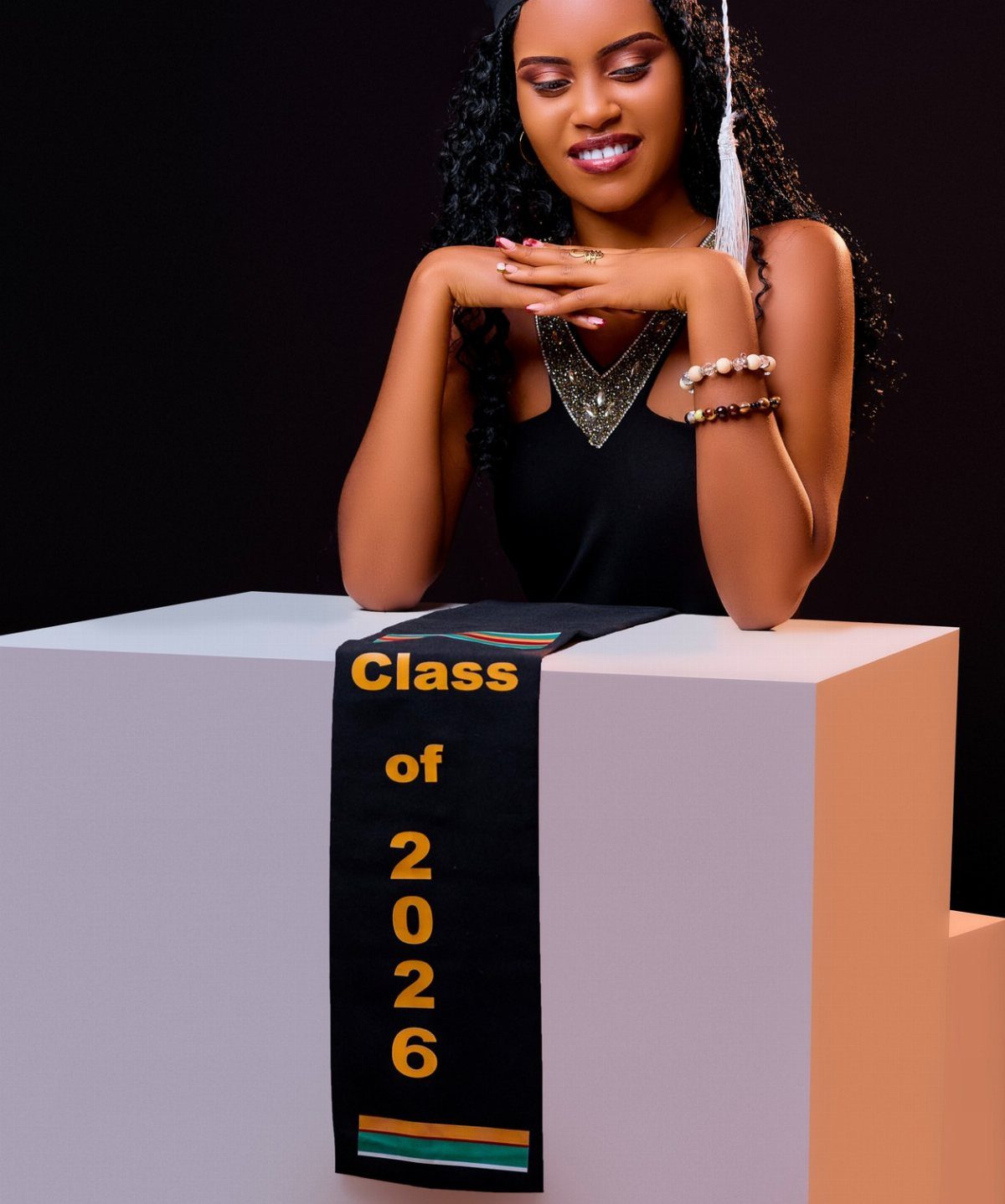 Young woman in graduation cap and dress posing with a Class of 2026 stole