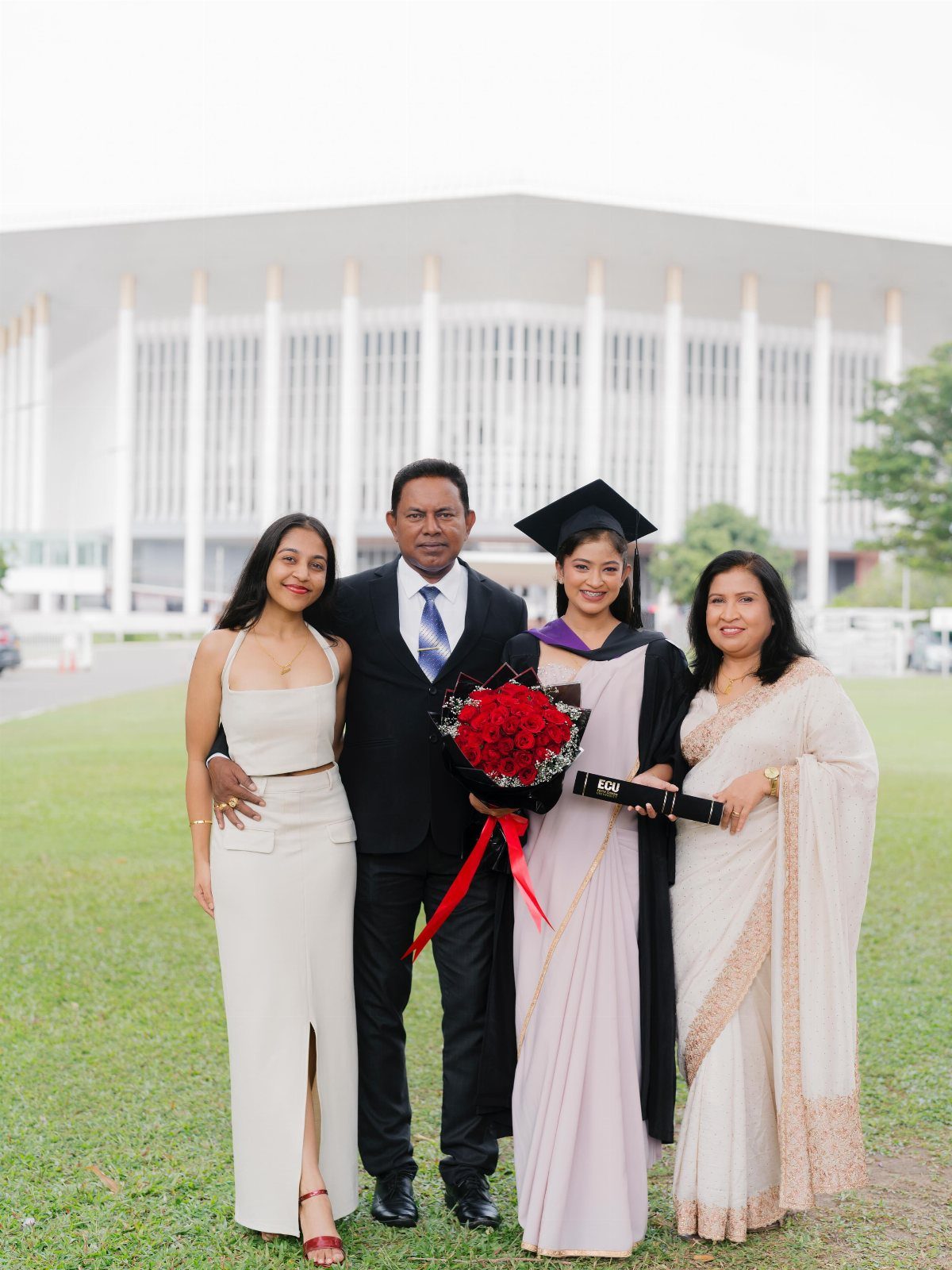Female graduate in cap and gown posing with her family in front of building