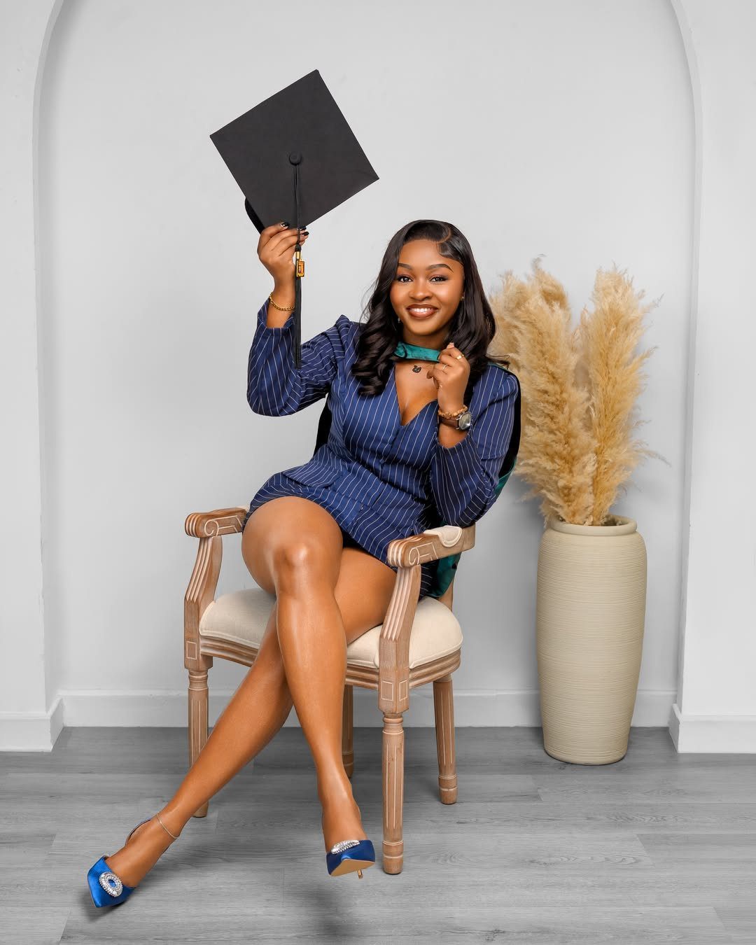 Woman in blue blazer dress sitting on a chair holding a graduation cap
