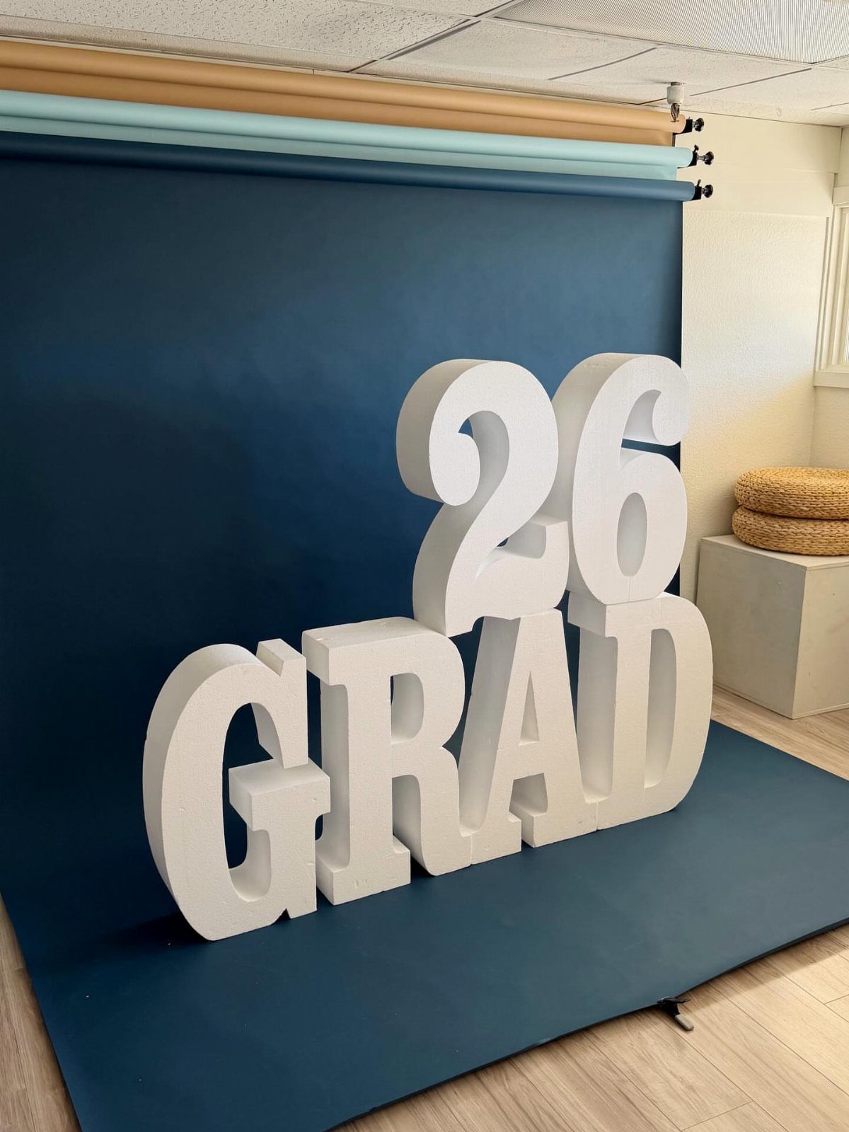 Large white 3D GRAD 26 letters against a dark blue studio backdrop.