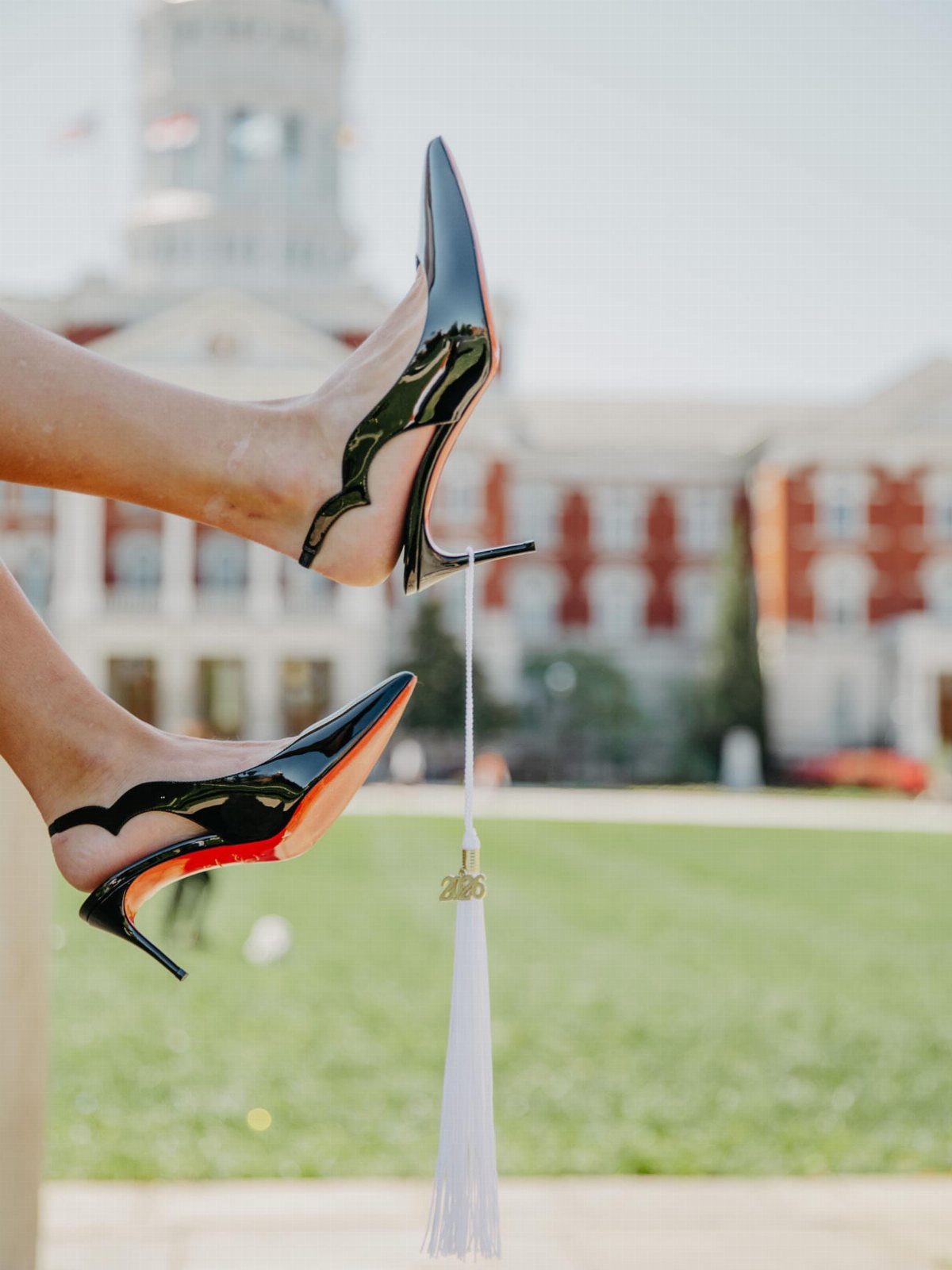 Black high-heeled shoes and a white graduation tassel against a blurred campus background.