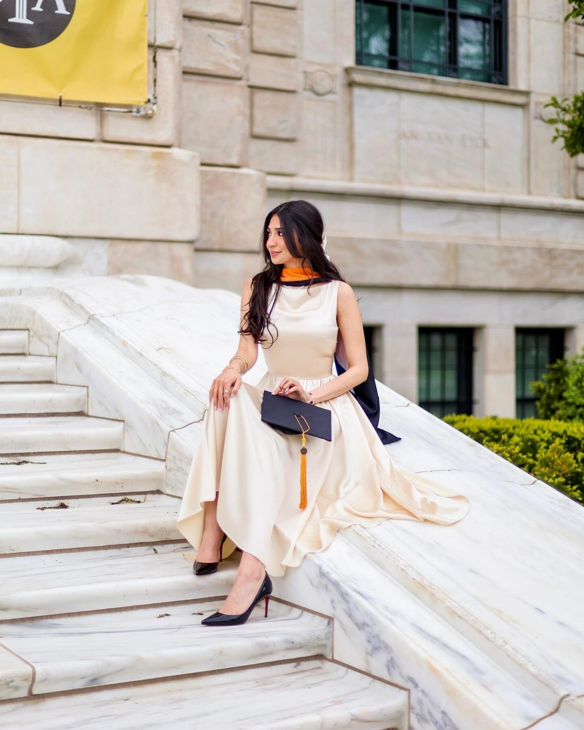 Woman in a cream dress sitting on white marble stairs before a building.