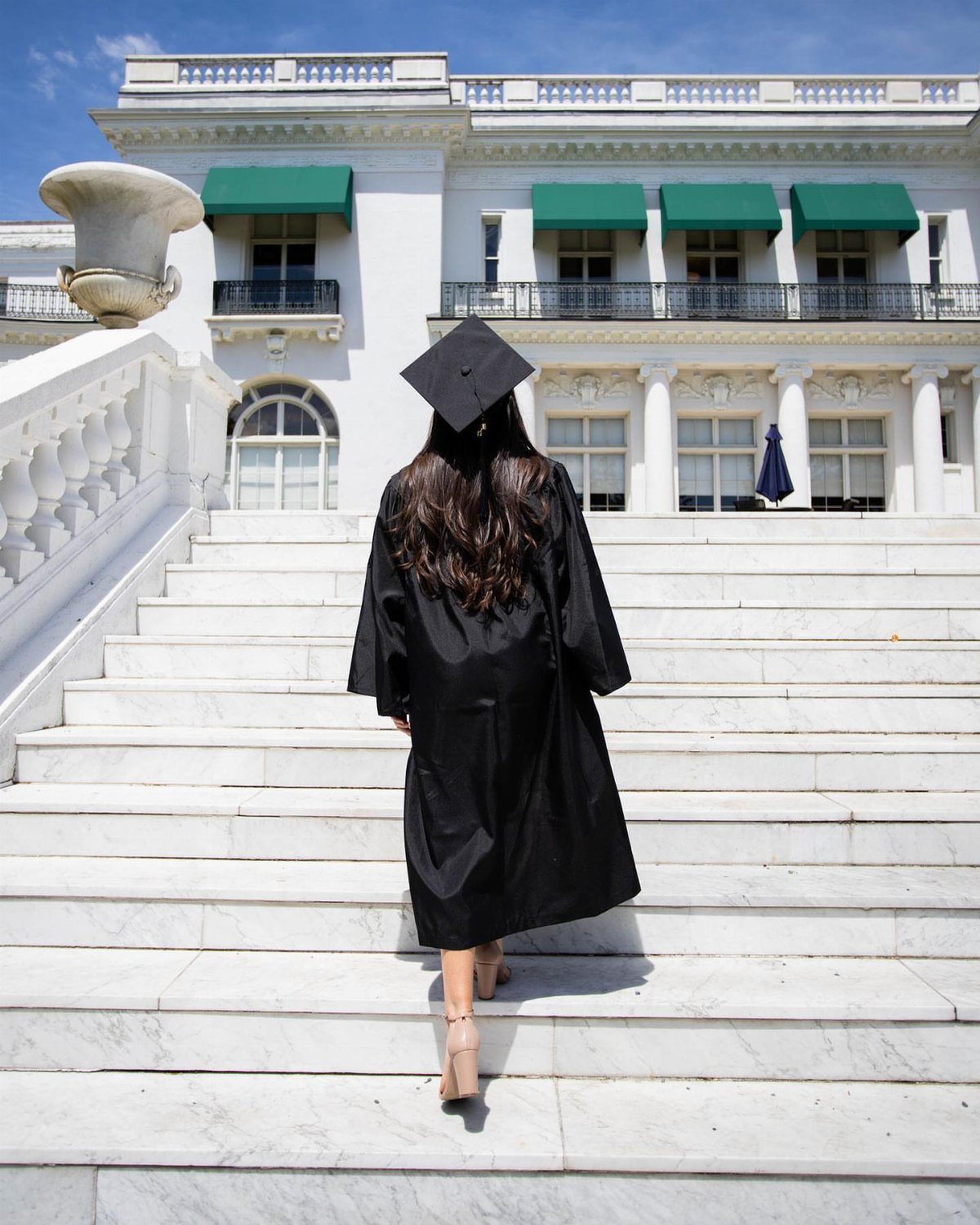 Graduate in black gown and cap walking up white marble stairs toward building