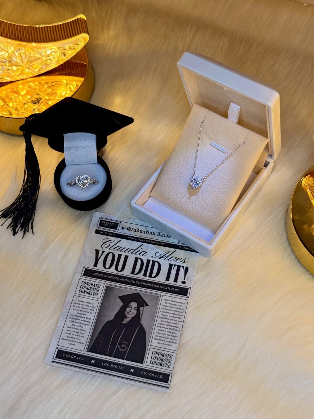 Graduation cap, jewelry boxes, and a personalized announcement card on white faux fur.