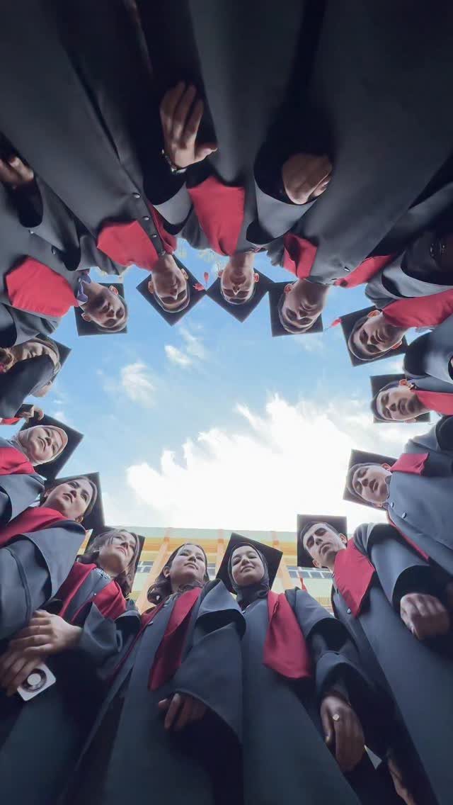 Graduates in black gowns and red stoles forming a circle looking down.