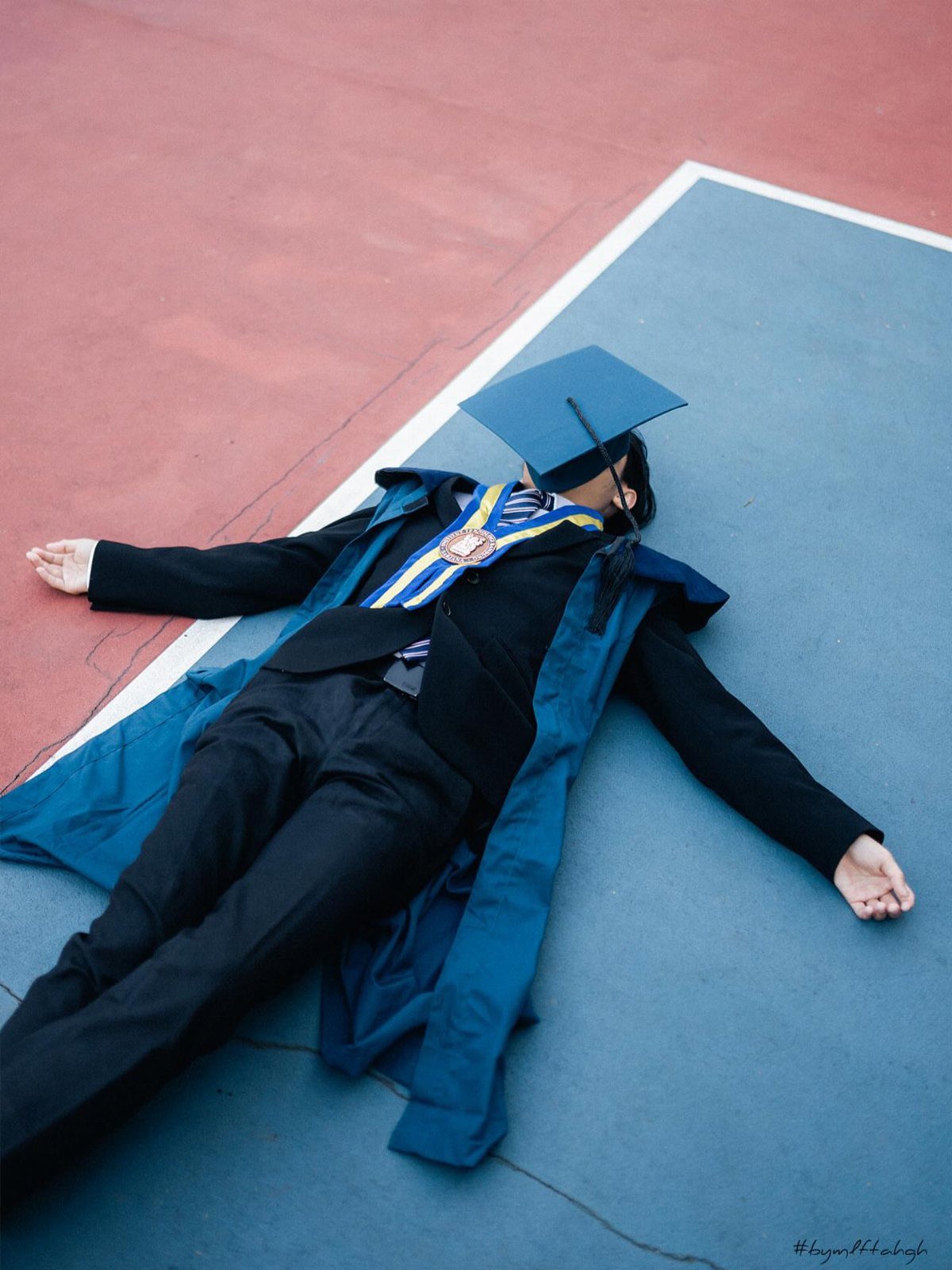 Graduate in cap and gown lying flat on a red and blue court.