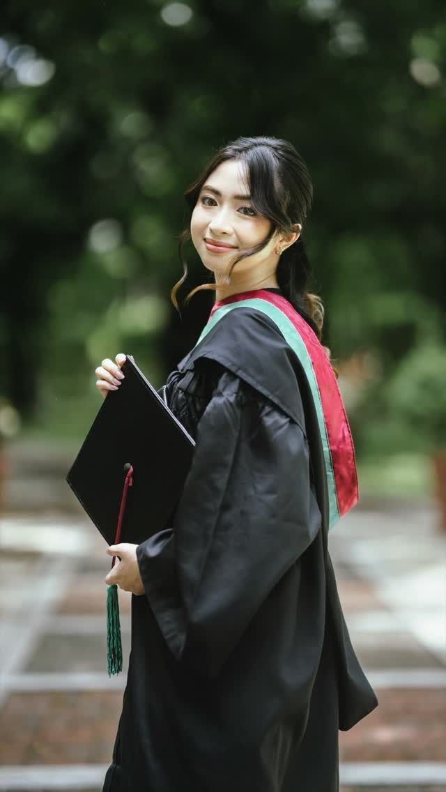 Graduating woman in black gown and stole holding her cap outdoors