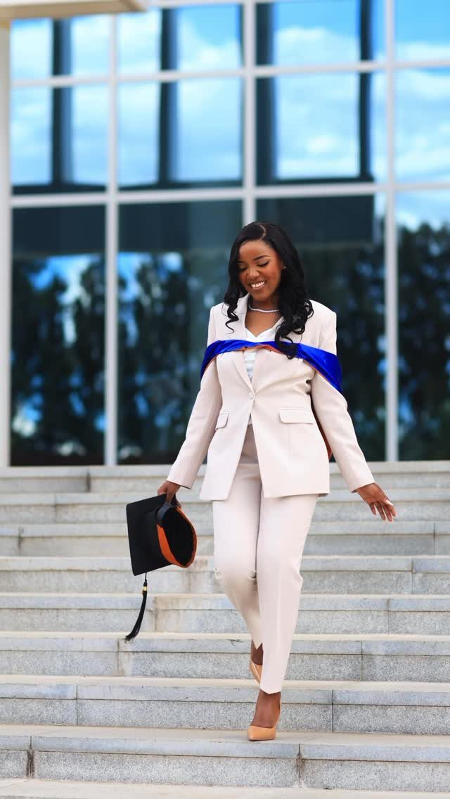 Woman in beige suit and blue graduation stole walking down concrete stairs.