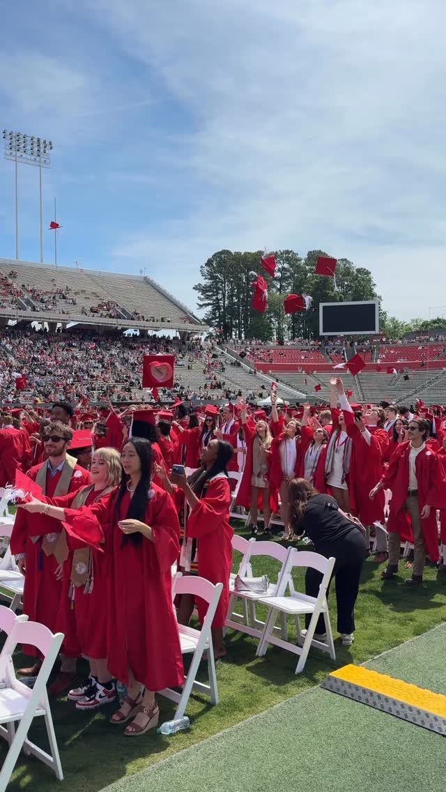 Graduates in red gowns tossing their caps into the air at a stadium.