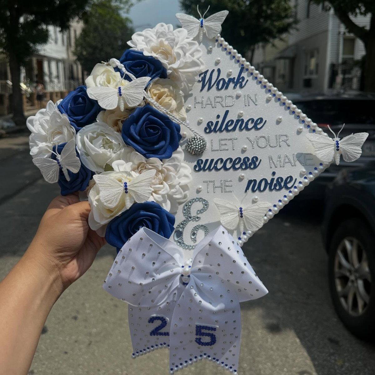 Decorated white graduation cap with blue roses, butterflies, and motivational quote.