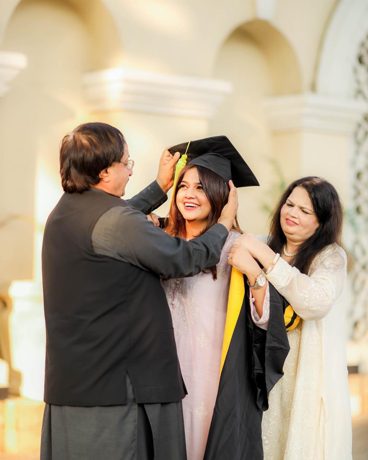 Man adjusting graduation cap on a smiling graduate while a woman looks on.